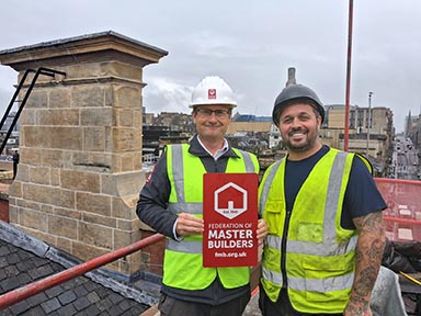 Two men in hi-vis jackets & hard hats on a rooftop.