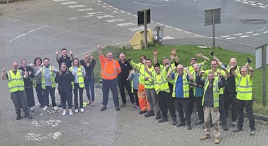 A group of more than 20 people in hi-vis jackets with arms raised.