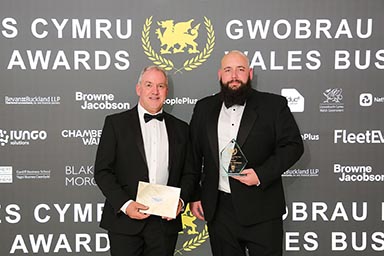 Two men dressed formally in front of a sign celebrating the Wales Business Awards 2026.