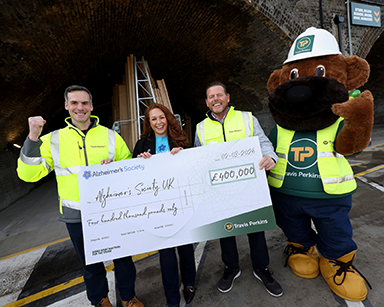 Two men, one woman and one mascot holding a large cheque made out for �400,000 in favour of Alzheimers Society UK on behalf of Travis Perkins.