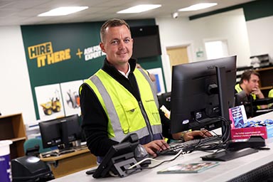 A man in a hi-vis jacket at a reception desk in a Travis Perkins branch.