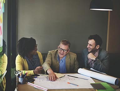 Three people sitting round a table with architect's plans on it.